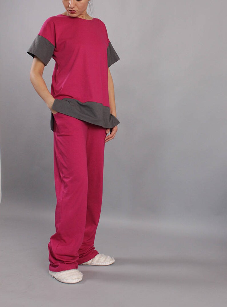 May include: A two-piece outfit in pink and gray. The top is a loose-fitting t-shirt with a gray band across the bottom. The pants are a relaxed fit with a straight leg.