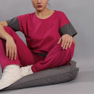 May include: A woman sits cross-legged on a gray cushion wearing a pink and gray pajama set. She is wearing white fuzzy socks.