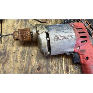 May include: A vintage Milwaukee power drill featuring a red plastic handle and a silver metal motor housing. The drill includes a rusted metal chuck at the front and a black trigger switch. The Milwaukee brand name is embossed on the side.