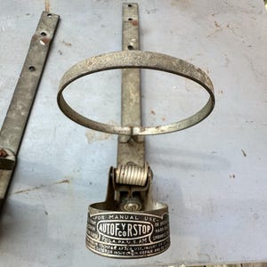 May include: An antique metal fire sprinkler system component. The device has a circular ring, a spring mechanism, and a cylindrical base with the text "AUTO-FYR-STOP" and other text. The metal has a weathered, aged appearance.