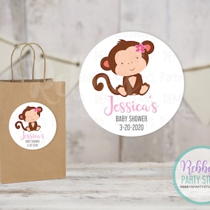 May include: A round sticker with a cartoon monkey wearing a pink flower. The sticker says "Jessica's Baby Shower 3-20-2020".