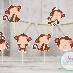 May include: Set of six brown monkey cupcake toppers with pink flowers. The monkeys are in various poses, including sitting, standing, and hanging upside down.