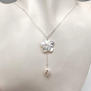 May include: A silver chain necklace with a silver flower pendant and a single white pearl dangling from the bottom.