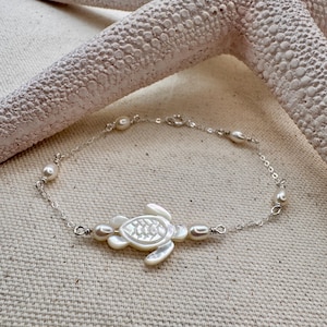 May include: A silver chain bracelet with white pearl accents and a white mother-of-pearl turtle charm.