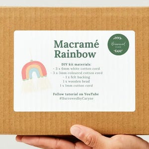 May include: A cardboard box with a label that says "Macrame Rainbow DIY kit materials:" and lists the materials needed to make a macrame rainbow. The label also includes the text "Follow tutorial on YouTube #BurrowedbyCaryne".
