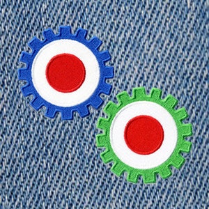 May include: Two colorful gear-shaped buttons with red, white, and blue and red, white, and green designs. The buttons are on a blue denim background.