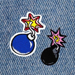Könnte beinhalten: Zwei gestickte Bügelbilder von Cartoon-Bomben. Eine Bombe ist blau mit einem gelben Stern und die andere ist schwarz mit einem rosa Stern.