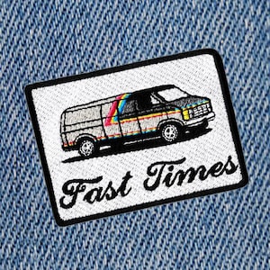 Puede incluir: Un parche blanco bordado con un contorno negro. El parche presenta una ilustración de dibujos animados de una camioneta blanca con rayas arcoíris y el texto "Fast Times" en una fuente cursiva negra.
