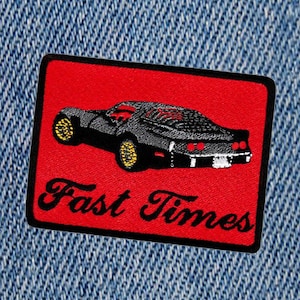Puede incluir: Parche bordado rojo y negro con un coche negro y el texto "Fast Times" en blanco.
