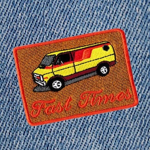 Puede incluir: Un parche bordado de color marrón y naranja con una furgoneta amarilla y el texto "Fast Times" en rojo.