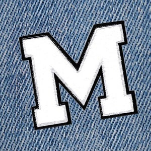 May include: White felt letter M with a black outline, sewn onto a blue denim fabric.
