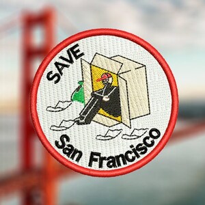 May include: A white embroidered patch with red stitching. The patch features a cartoon illustration of a person sitting inside a box with the words "SAVE San Francisco" around the image.