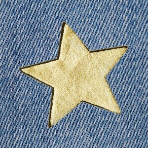 Peut inclure: Gros plan sur un tissu denim bleu avec une découpe en forme d'étoile dorée. L'étoile a un aspect texturé, contrastant avec le denim lisse. L'image met en évidence le contraste de texture et de couleur.