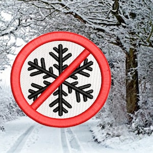May include: A red circle with a diagonal line through a black snowflake. The sign is in a snowy forest setting.