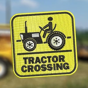 May include: Embroidered yellow patch with a black tractor graphic and the words "TRACTOR CROSSING". The patch features a black tractor silhouette with a driver. The background is a blurred image of a field and a tractor.