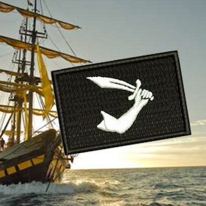 Puede incluir: Una bandera pirata en blanco y negro con un brazo estilizado sosteniendo una espada. La bandera ondea en un barco alto con velas amarillas.