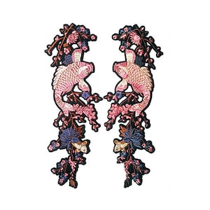 Könnte beinhalten: Zwei gestickte Aufnäher mit rosa und weißen Koi-Karpfen mit schwarzen Umrissen. Die Fische sind von rosa und violetten Blumen und Blättern umgeben. Die Aufnäher eignen sich perfekt, um Kleidung, Taschen oder anderen Bastelarbeiten einen Hauch von asiatisch inspiriertem Stil zu verleihen.