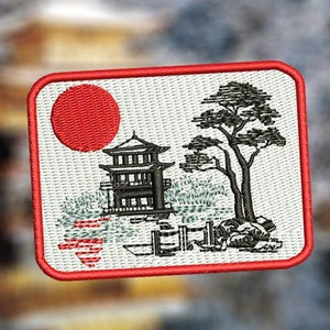 May include: An embroidered patch featuring a Japanese-style scene. The patch is red, white and black and depicts a red sun, a small building with a tiered roof, a tree and a fence.