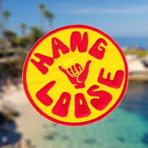Puede incluir: Un parche redondo amarillo y rojo con el texto "HANG LOOSE" en letras rojas y una mano roja haciendo el signo shaka en el centro.
