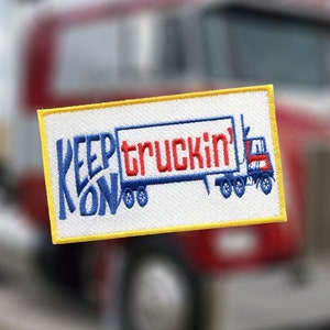Puede incluir: Un parche bordado blanco con borde amarillo. El parche presenta un camión semi-remolque azul y rojo con el texto "KEEP ON TRUCKIN'" en letras azules y rojas.
