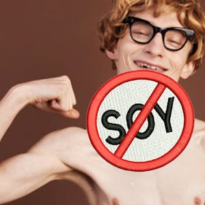 May include: A man with red hair and glasses flexes his bicep while holding a red circle with a diagonal line through it and the word "SOY" in black text.
