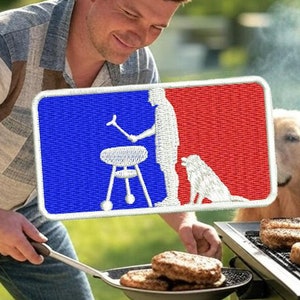Puede incluir: Un hombre asando hamburguesas en una parrilla de gas negra con un perro golden retriever observando. El hombre lleva una camisa a cuadros azul y blanca y pantalones vaqueros azules. Un parche blanco con un diseño rojo, blanco y azul es visible en la camisa del hombre. El parche representa a una persona asando a la parrilla con un perro de pie junto a ella.