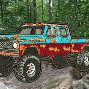 Pode incluir: Um remendo bordado de uma caminhonete azul e vermelha enferrujada com pneus grandes, contra um fundo de floresta verde.