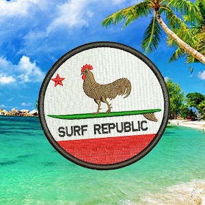 May include: A round embroidered patch with a white background, a red star, a brown rooster standing on a green surfboard, and the text "SURF REPUBLIC" in black. The patch is set against a backdrop of a tropical beach scene with palm trees and blue sky.