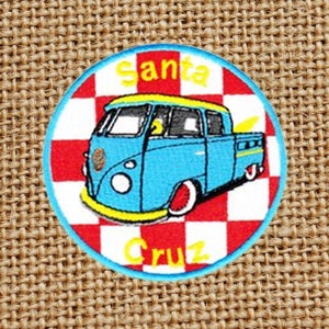 Peut inclure: Un patch brodé bleu et jaune avec un fond à carreaux rouge et blanc. Le patch représente un van bleu avec une bande jaune et le texte "Santa Cruz".