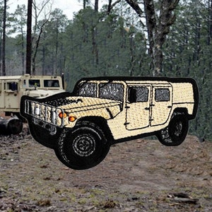 Puede incluir: Un Humvee militar beige con neumáticos negros y un contorno negro. El Humvee se encuentra en una zona boscosa con un soldado con uniforme de camuflaje de pie en primer plano.