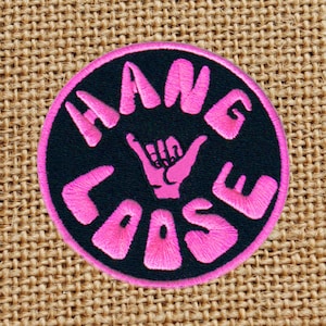 Może przedstawiać: Naszywka haftowana na różowo i czarno z napisem "Hang Loose" i różowym gestem dłoni.