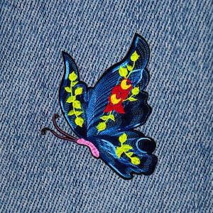 May include: A blue butterfly embroidered patch with yellow and red floral details on a denim background.