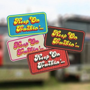 Puede incluir: Cuatro parches bordados con el texto "Keep On Truckin'" en una fuente retro. Los parches son de diferentes colores: azul, beige, negro y rojo.