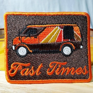 Puede incluir: Un parche bordado con una furgoneta vintage con un diseño a rayas de colores y el texto "Fast Times" en letras naranjas sobre un fondo marrón.