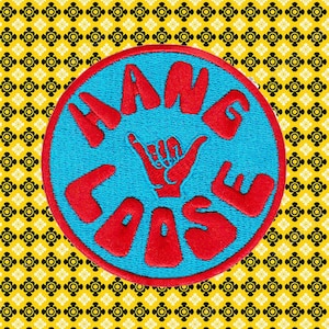Op de afbeelding: Een blauwe en rode geborduurde patch met de tekst "Hang Loose" in een cirkel. De tekst is in een rood, cursief schrift met een handgebaar in het midden.