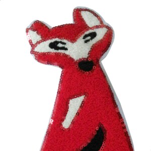 Peut inclure: Applique de renard rouge en paillettes avec des détails noirs. Le renard est debout sur ses pattes arrière avec sa queue enroulée autour de son corps.