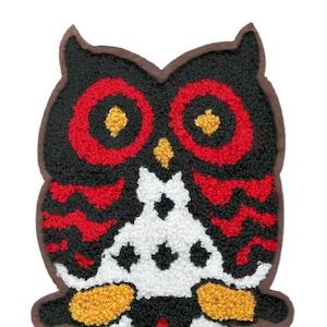 May include: A black, red, and white owl applique with a brown outline. The owl has large, round eyes with yellow centers.