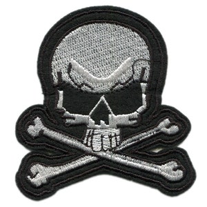 Puede incluir: Parche bordado en blanco y negro con una calavera y huesos cruzados. La calavera es blanca con ojos negros y un contorno negro. Los huesos cruzados son blancos con un contorno negro.