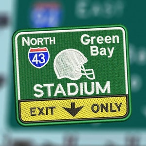 Puede incluir: Un letrero verde y amarillo con el texto "North Green Bay Stadium Exit Only" y un gráfico de casco de fútbol blanco. El letrero también incluye un letrero de carretera con el número 43.