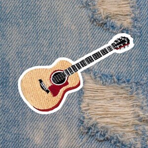May include: A guitar-shaped patch with a light brown body, red accents, and a black fretboard. The patch is outlined in white and is set against a distressed denim background.