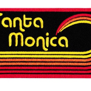 Puede incluir: Parche bordado con la inscripci&oacute;n "Santa Monica" en amarillo, en forma de arco. El parche tiene un fondo negro con rayas amarillas, naranjas y rojas y un borde rojo. El dise&ntilde;o incluye un arco&iacute;ris estilizado.