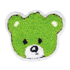 Może przedstawiać: Zielony, pluszowy naszywkę z haftowanym motywem głowy niedźwiedzia, z białym obramowaniem i czarnymi oczami.