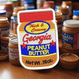 Puede incluir: Un parche bordado blanco, rojo, amarillo y azul de un tarro de mantequilla de cacahuete. El tarro tiene el texto "Thick & Creamy Georgia Peanut Butter Net Wt. 16oz."
