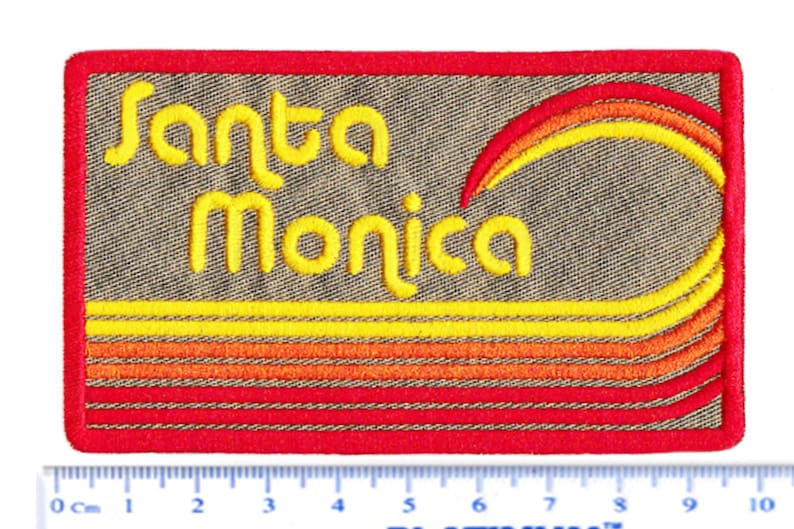 Puede incluir: Parche bordado con las palabras "Santa Monica" en escritura amarilla. El parche presenta un dise&ntilde;o de l&iacute;neas horizontales amarillas, naranjas y rojas y un arco&iacute;ris curvo. El parche es rectangular con un borde rojo.