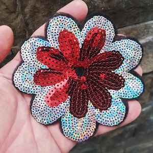 May include: A red and silver sequin flower applique with a black mesh backing. The flower has a five-petal design and is perfect for adding a touch of sparkle to clothing or crafts.