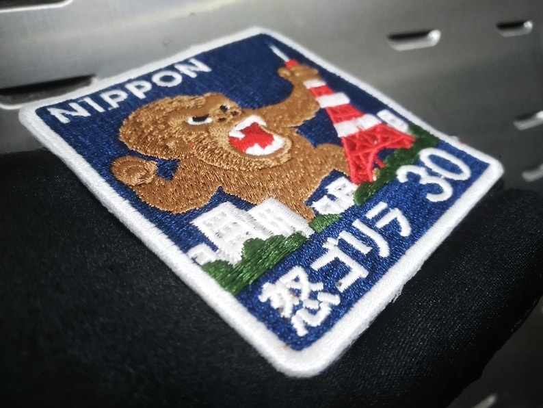 May include: Embroidered patch with a blue background and white border. The patch features a brown gorilla, a red and white tower, and the text "NIPPON" and "怒りゴリラ 30".