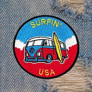 Puede incluir: Un parche bordado de color rojo, blanco y azul con una furgoneta Volkswagen vintage y una tabla de surf. El parche dice "SURFIN' USA" en letras amarillas.