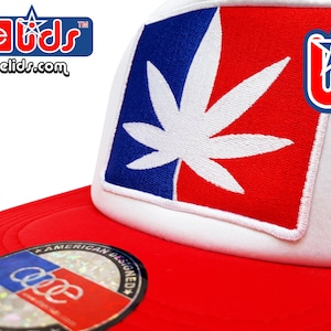 May include: Red and white trucker hat with a cannabis leaf design. The leaf is white, set against a blue and red background. The hat features the text "dope lids" and "dopelids.com".