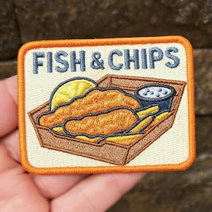 Może przedstawiać: Wyszywana naszywka w kształcie prostokąta z niebieskim napisem "FISH & CHIPS". Przedstawia porcję fish and chips, plaster cytryny i mały pojemnik z sosem tatarskim. Naszywka ma pomarańczową obwódkę.