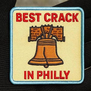 May include: Embroidered patch with a cream background, blue border, and the text "BEST CRACK IN PHILLY" in red. The patch features a detailed illustration of the Liberty Bell in shades of brown and gold.